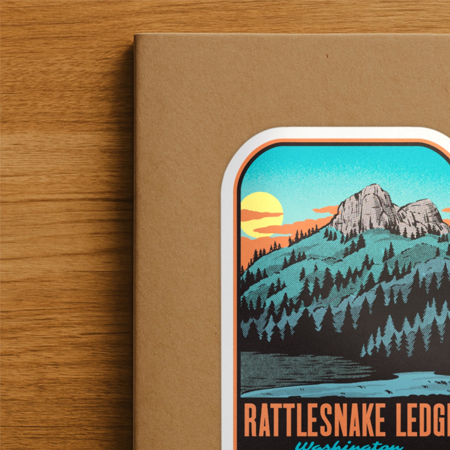 Notebook with a mountain illustration and 'Rattlesnake Ledge, Washington' text on a wooden surface
