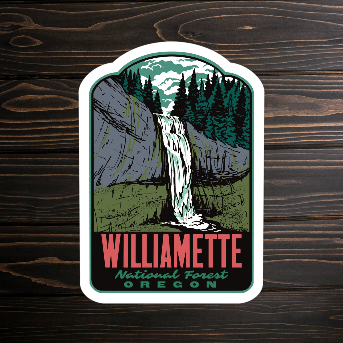 A die-cut sticker featuring an illustration of the Williamette National Forest waterfall in Oregon, displayed on a dark wood background.