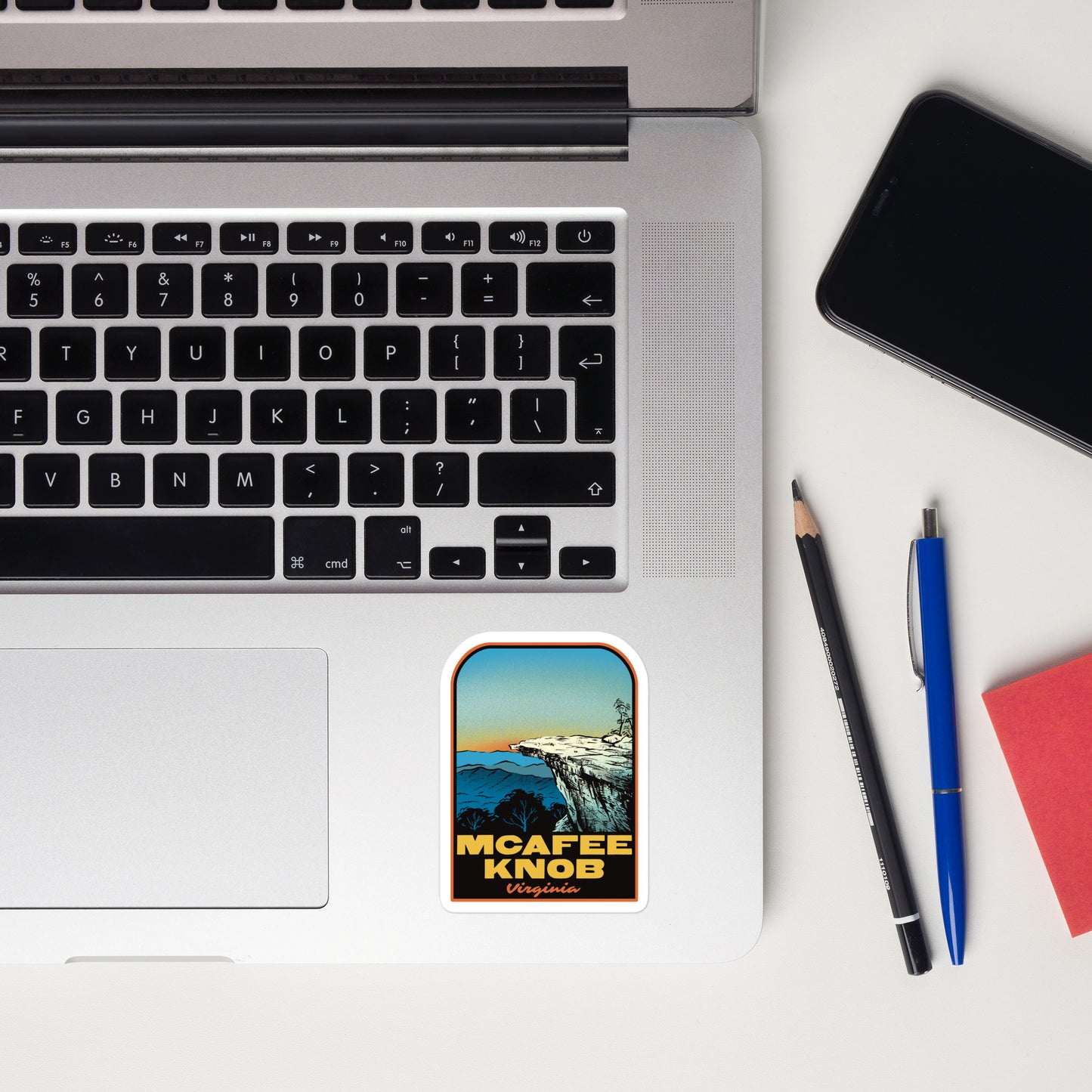 Laptop with a sticker on a desk next to a phone, pencil, and pen