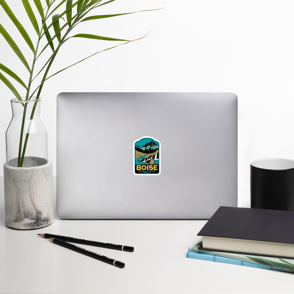 Laptop with a colorful Boise Idaho sticker on a desk with a plant, pencils, and books.