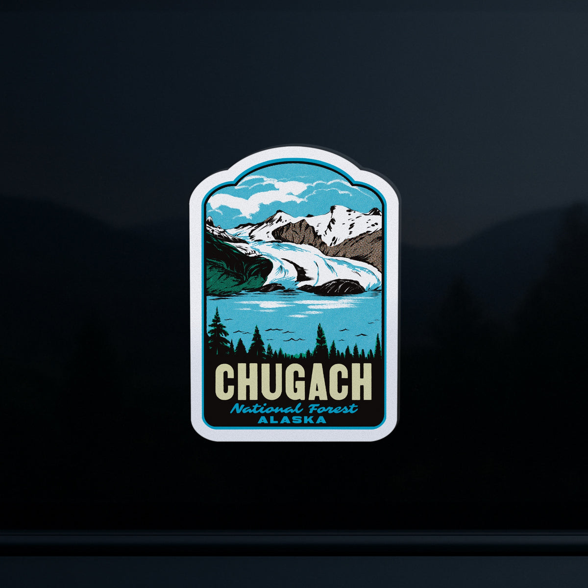 A die-cut sticker featuring a stylized illustration of Chugach National Forest in Alaska, with mountains, a glacier, trees, and the text 'CHUGACH National Forest ALASKA', shown against a dark reflective background.