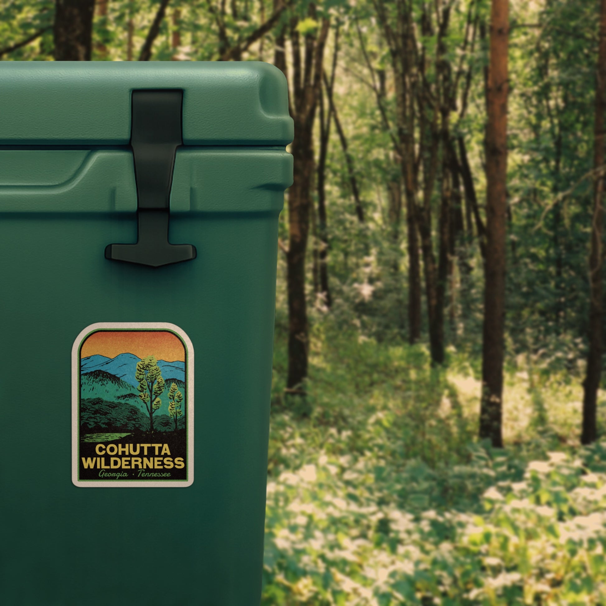 A retro vinyl sticker of Cohutta Wilderness stuck to a cooler in a green forest