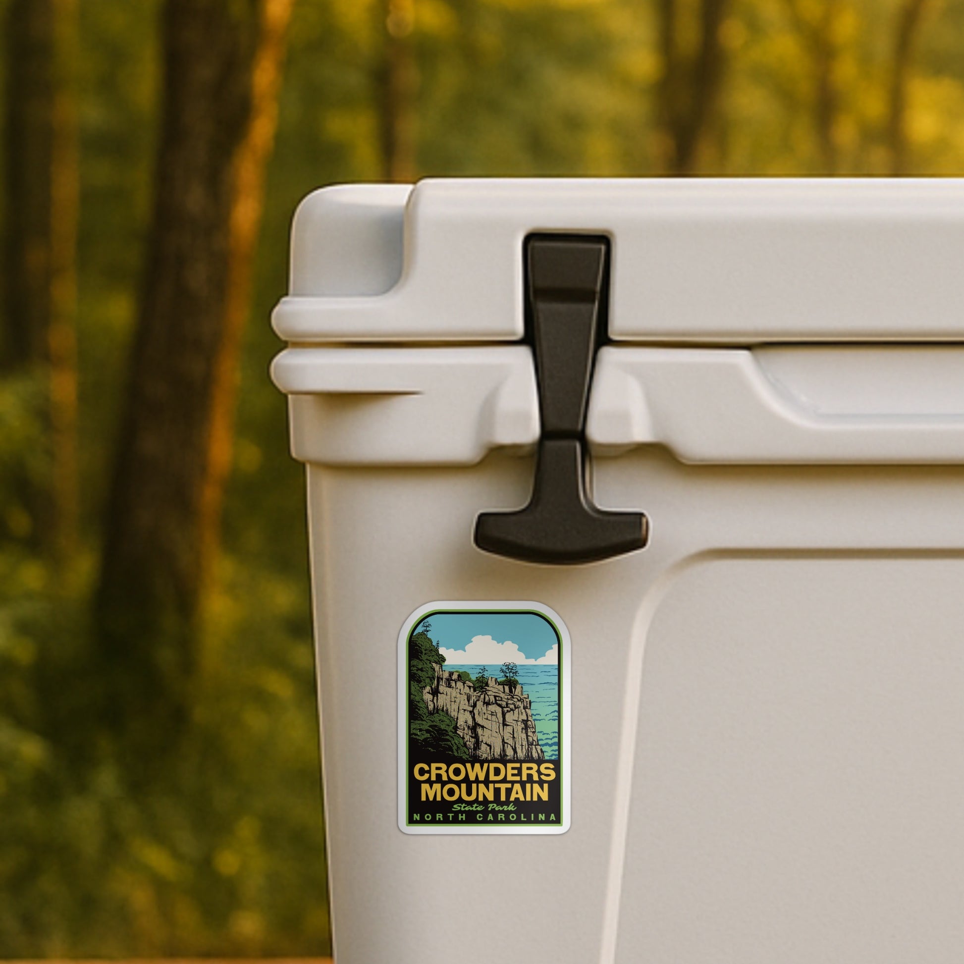 Beige cooler with a 'Crowders Mountain' sticker in a forest setting