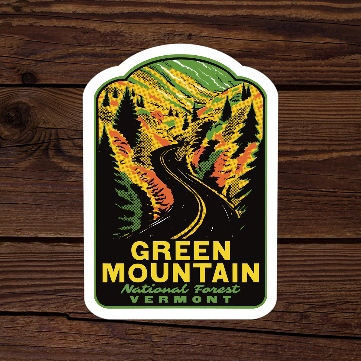 A die-cut sticker featuring a retro-style illustration of a winding road through autumn-colored mountains and forests, with the text 'GREEN MOUNTAIN National Forest VERMONT' on a dark wood background.