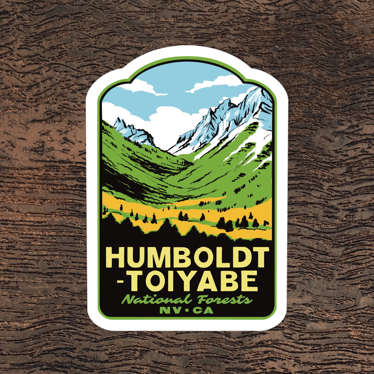 A die-cut sticker featuring a stylized mountain landscape with green hills, yellow fields, blue sky, and white snow-capped peaks. The text reads “HUMBOLDT - TOIYABE National Forests NV • CA” in yellow and green.