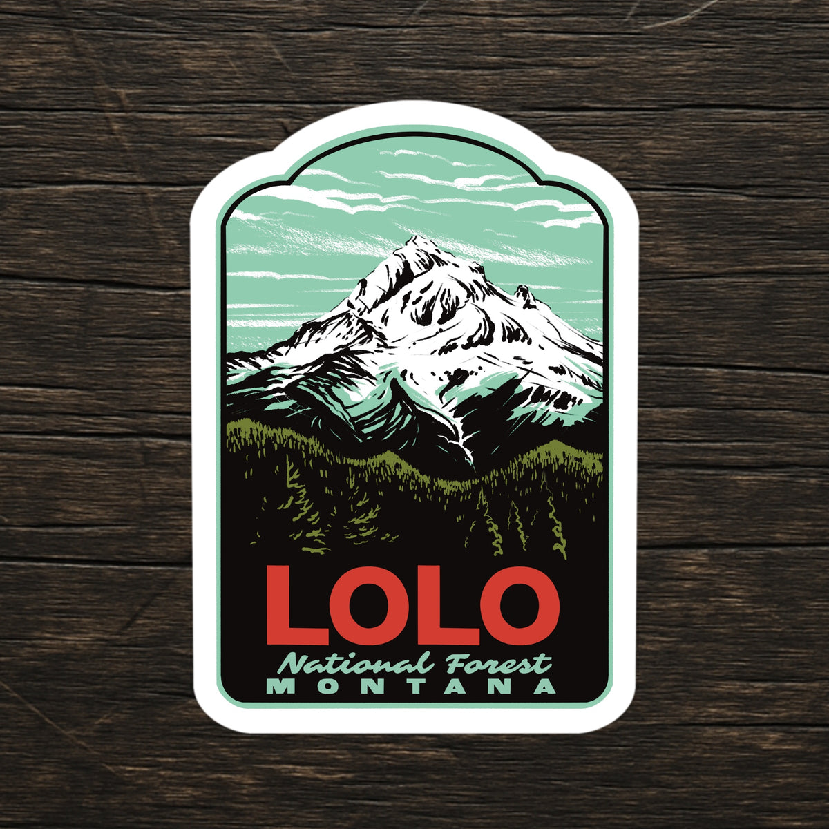 A die-cut sticker featuring a stylized mountain illustration with the text 'LOLO National Forest MONTANA,' shown on a dark wood background.