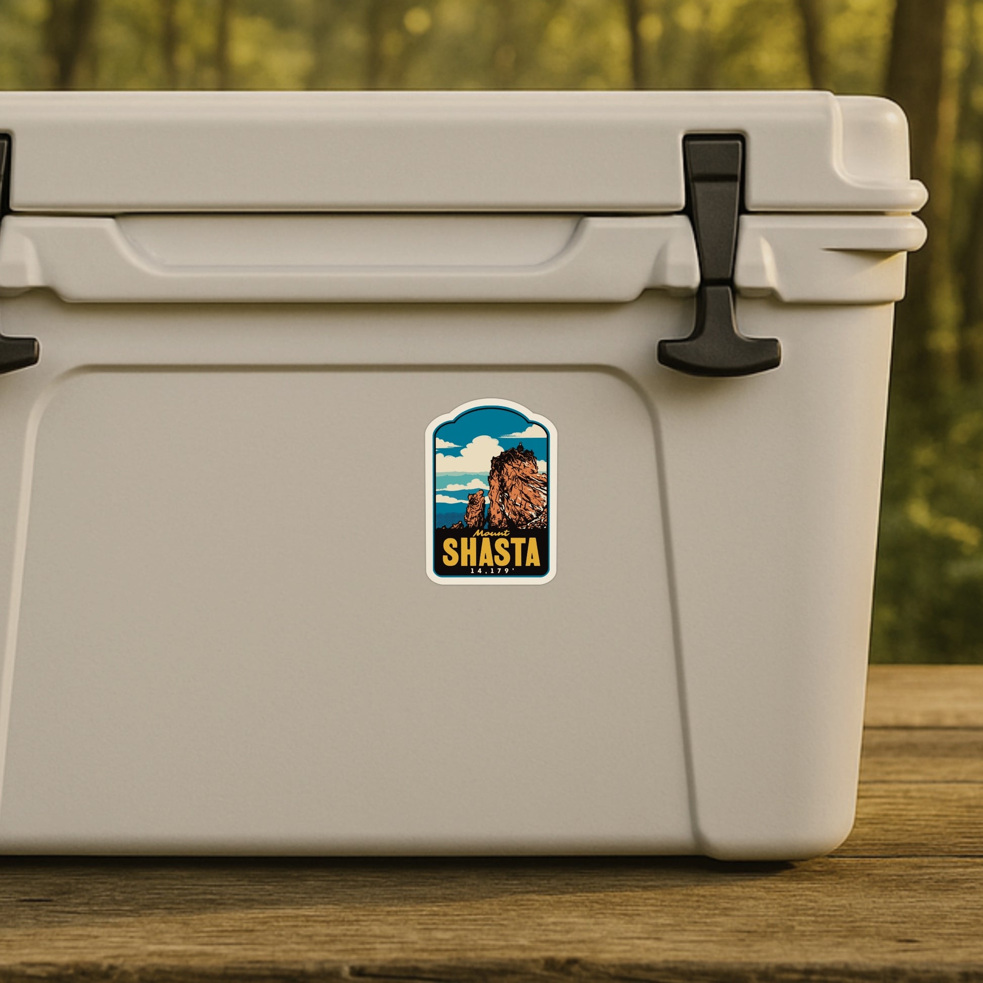 Beige cooler with a Mount Shasta sticker on a wooden surface with a blurred natural background