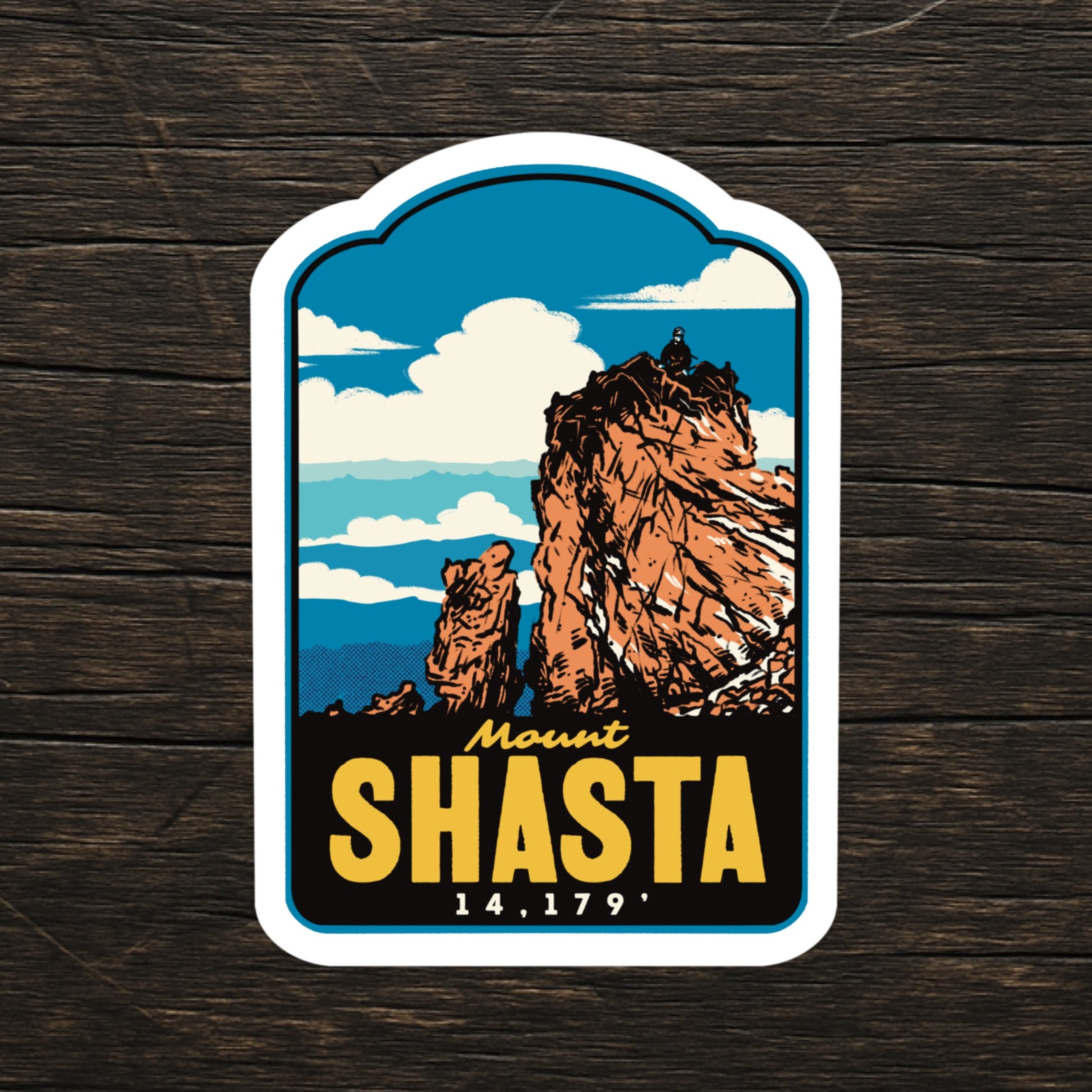 A die-cut sticker featuring a retro-style illustration of Mount Shasta, displayed on a dark wood background. The sticker has a white border and displays the text 'Mount SHASTA 14,179' in yellow and white lettering.