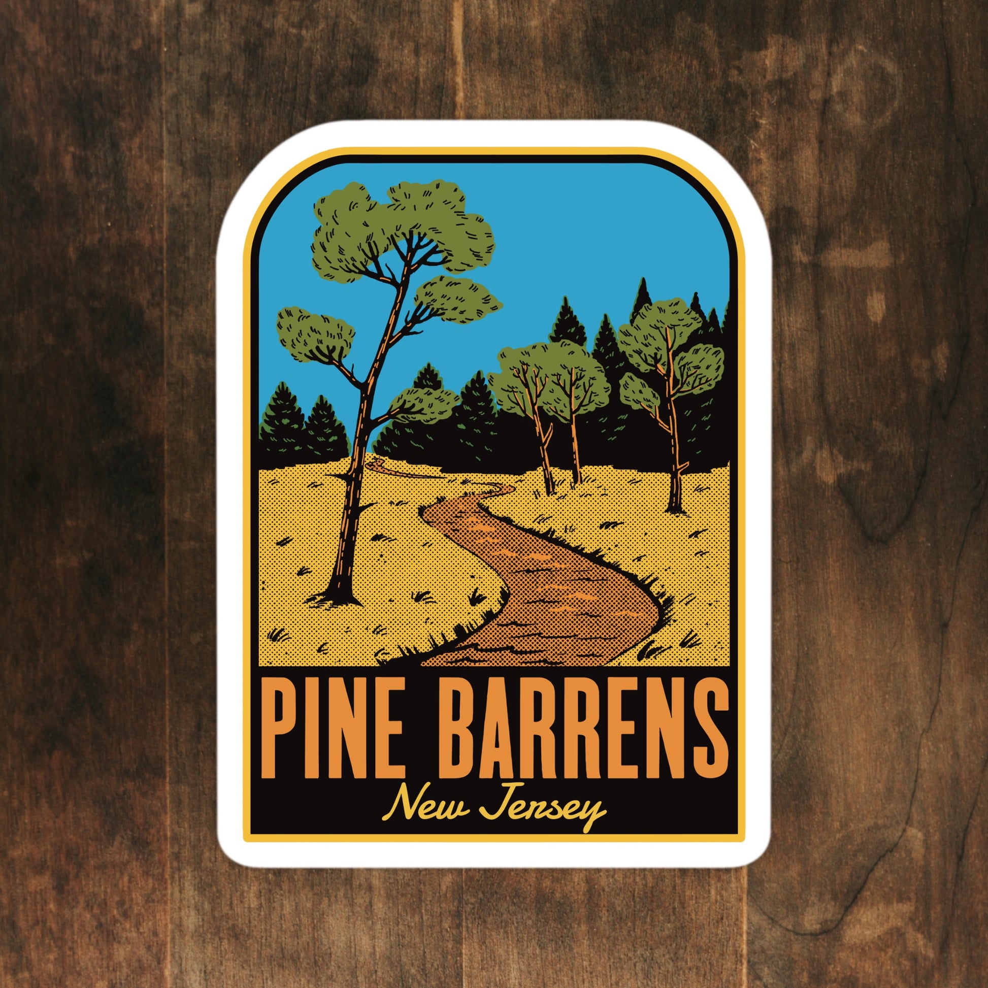 Sticker with illustration of a path through trees and text 'Pine Barrens New Jersey' on a wooden background