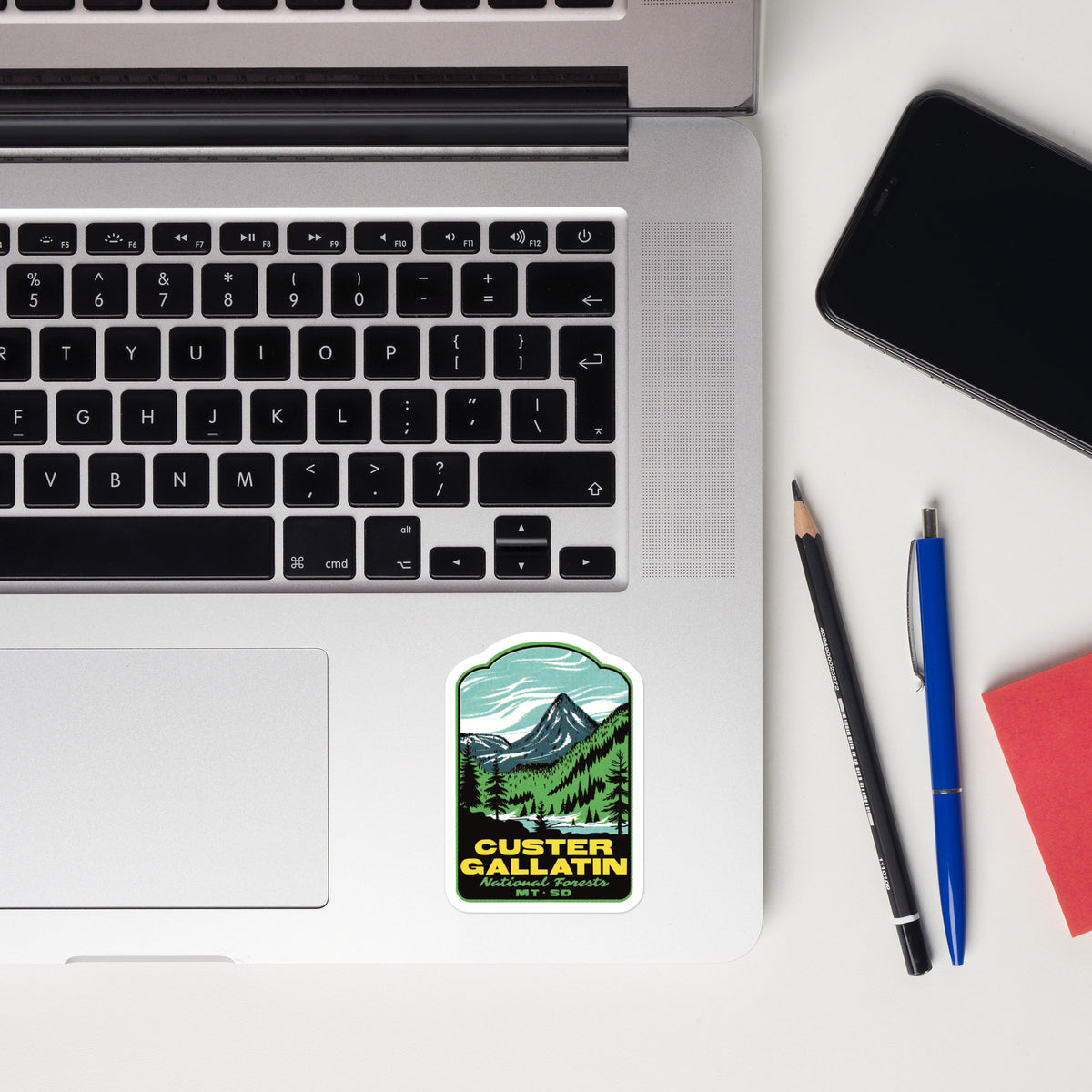 A rectangular sticker with an arched top featuring a retro-style illustration of Cleveland, Ohio, placed on the bottom right corner of a silver laptop. The sticker depicts a blue sky, a dark mountain peak, and a brown landscape with the word 'CLEVELAND' in orange.