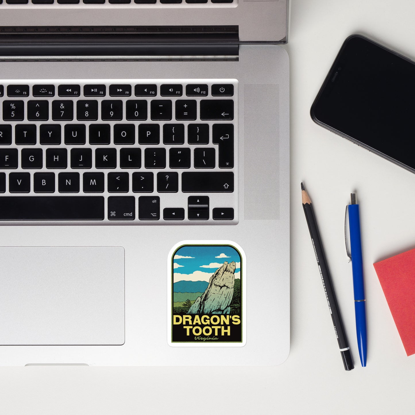 Laptop with 'Dragon's Tooth' sticker, phone, pencil, and pen on a white surface