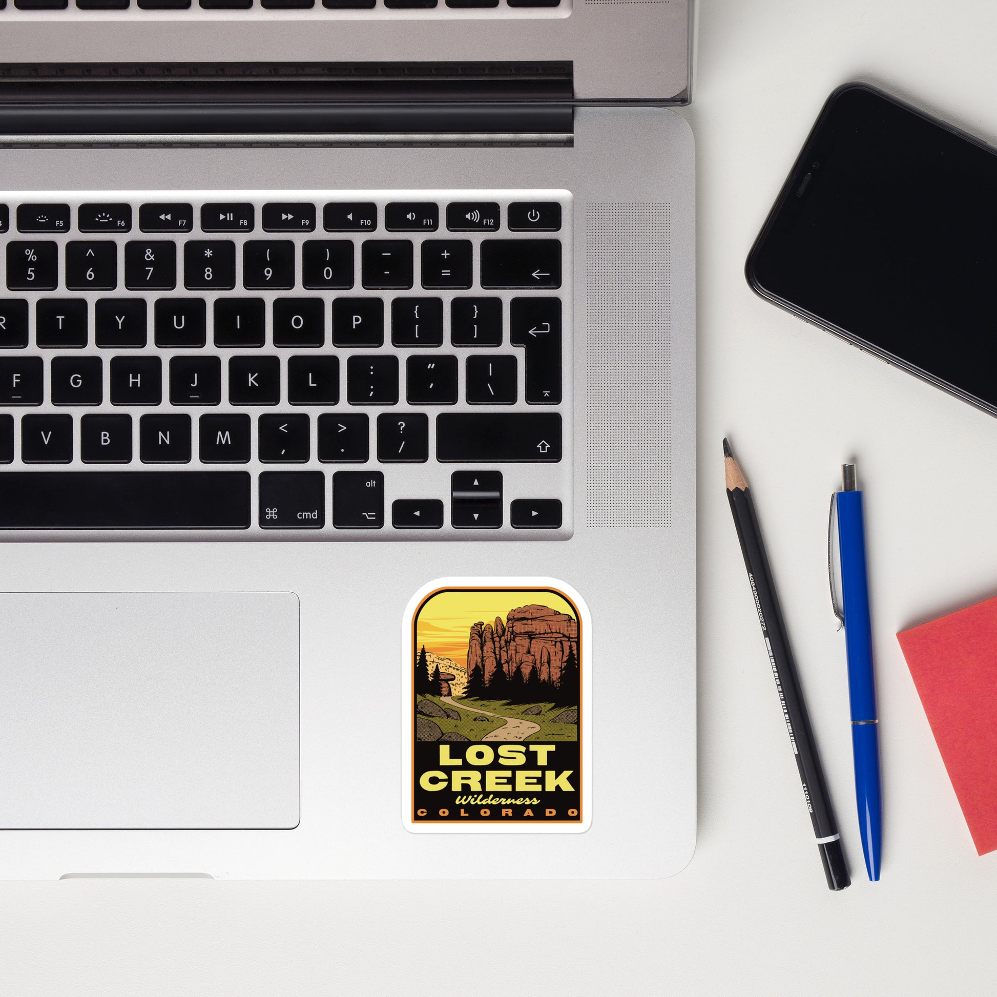 Laptop with a 'Lost Creek' sticker, phone, pencil, and pen on a white surface