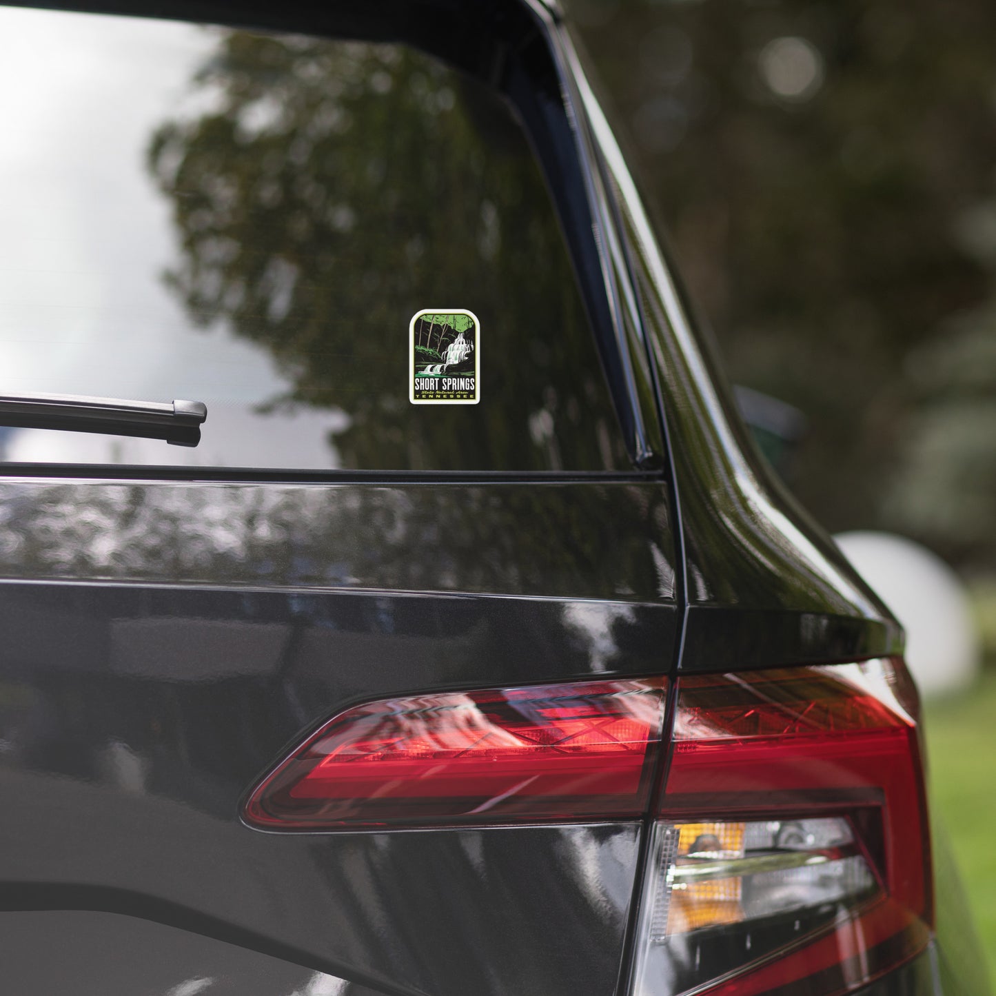 Car with a sticker on the rear window, surrounded by trees