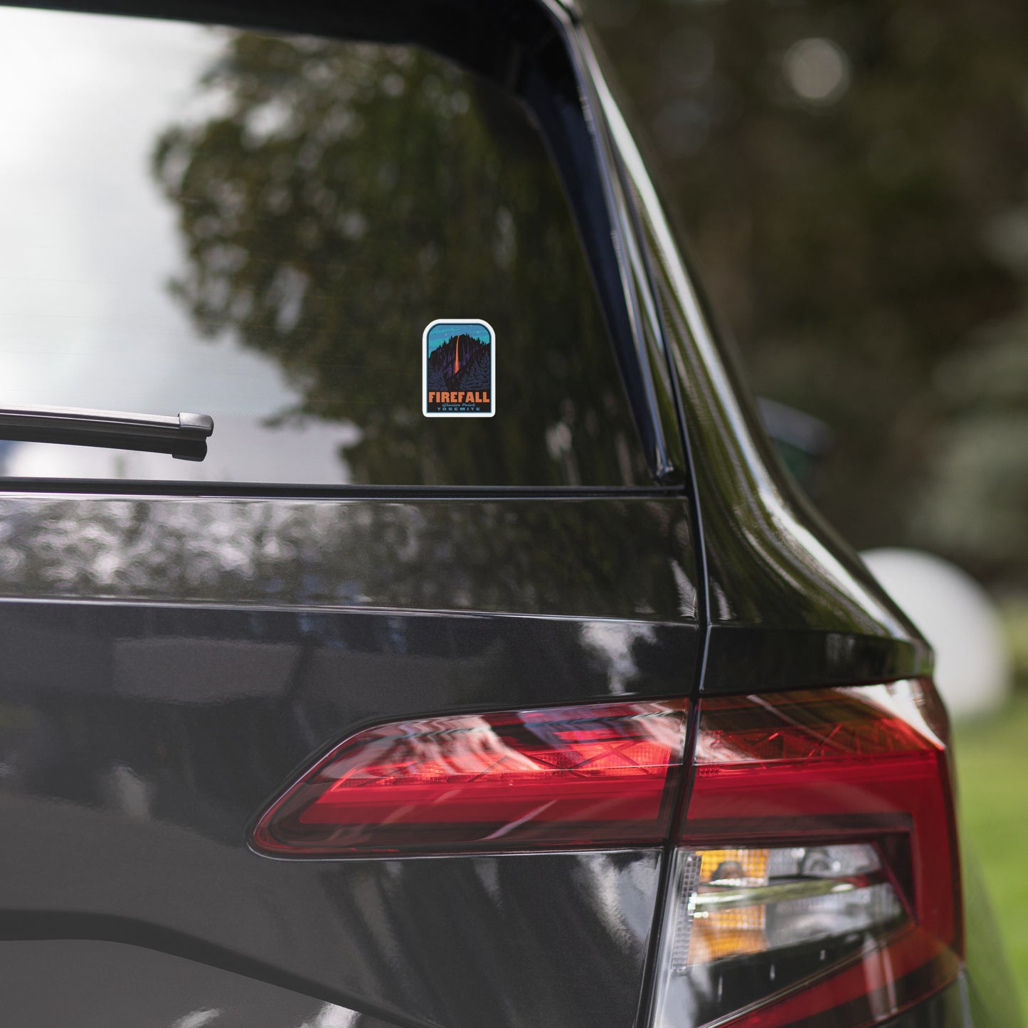 Car's rear view with a blue decal on the window, blurred greenery in the background