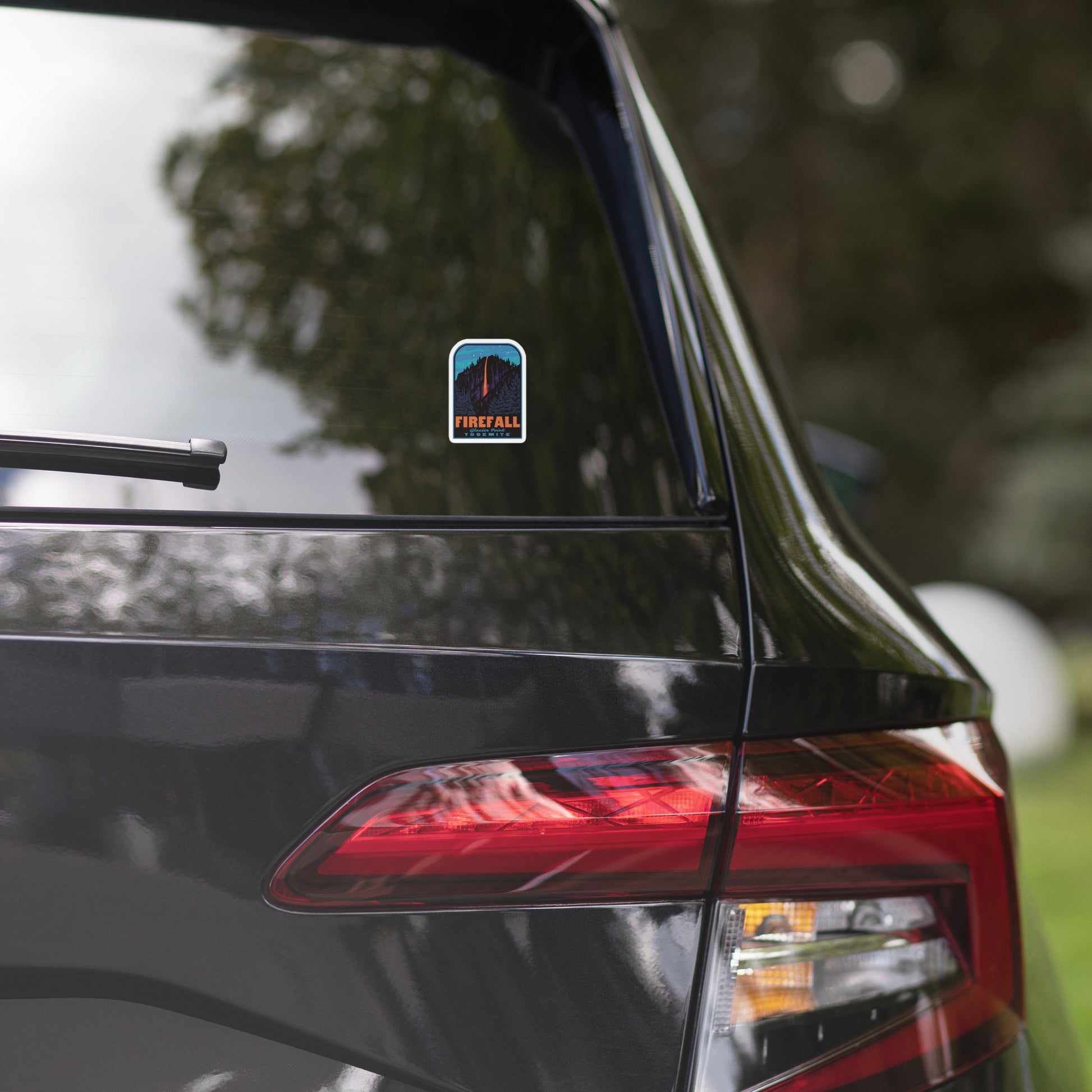 Car's rear view with a blue decal on the window, blurred greenery in the background